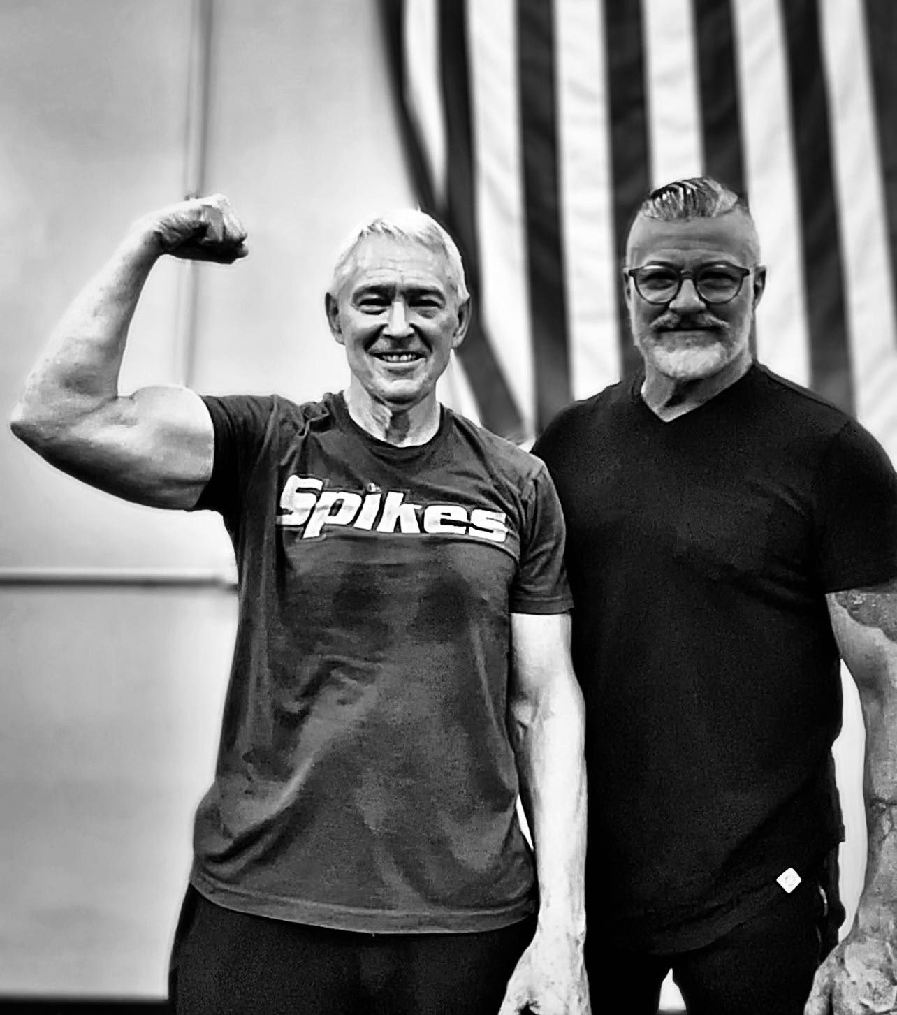 Mark McIntosh with client Tom in Spikes t-shirt flexing in front of American flag - black and white photo